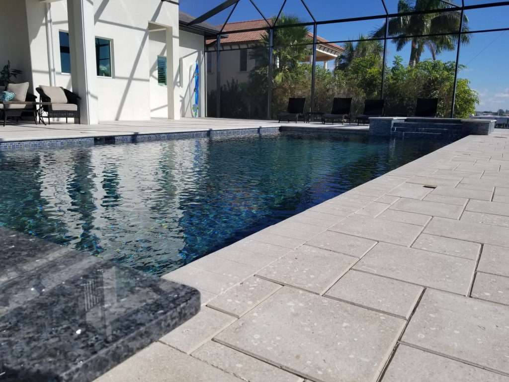 Clear blue pool with elegant stone patio and screened enclosure, set in a sunny outdoor space.