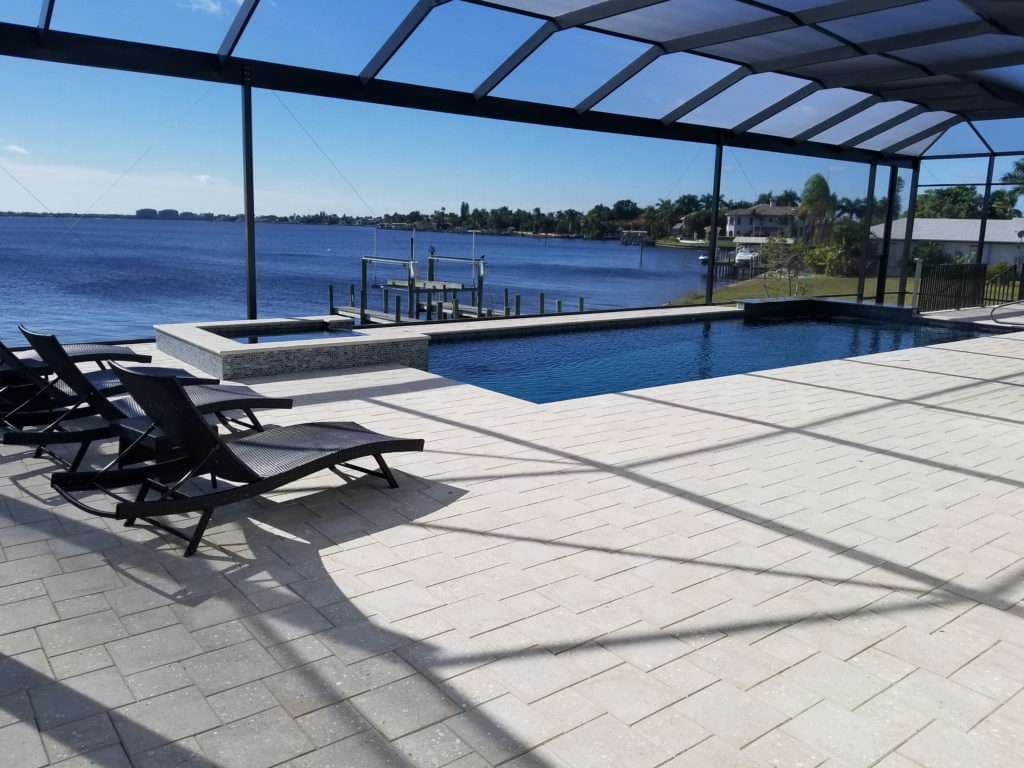 Modern pool overlooking a scenic lake, featuring lounge chairs and a spa area.