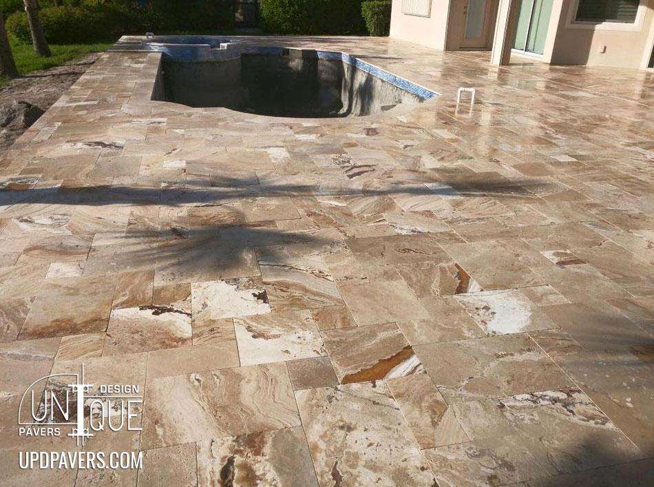 Elegant travertine paver patio surrounding a pool with a modern design and stone texture.