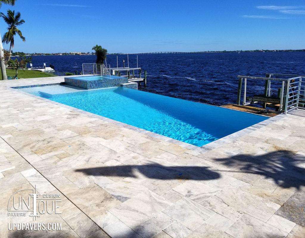 Luxury infinity pool overlooking water with modern landscaping and clear blue sky.