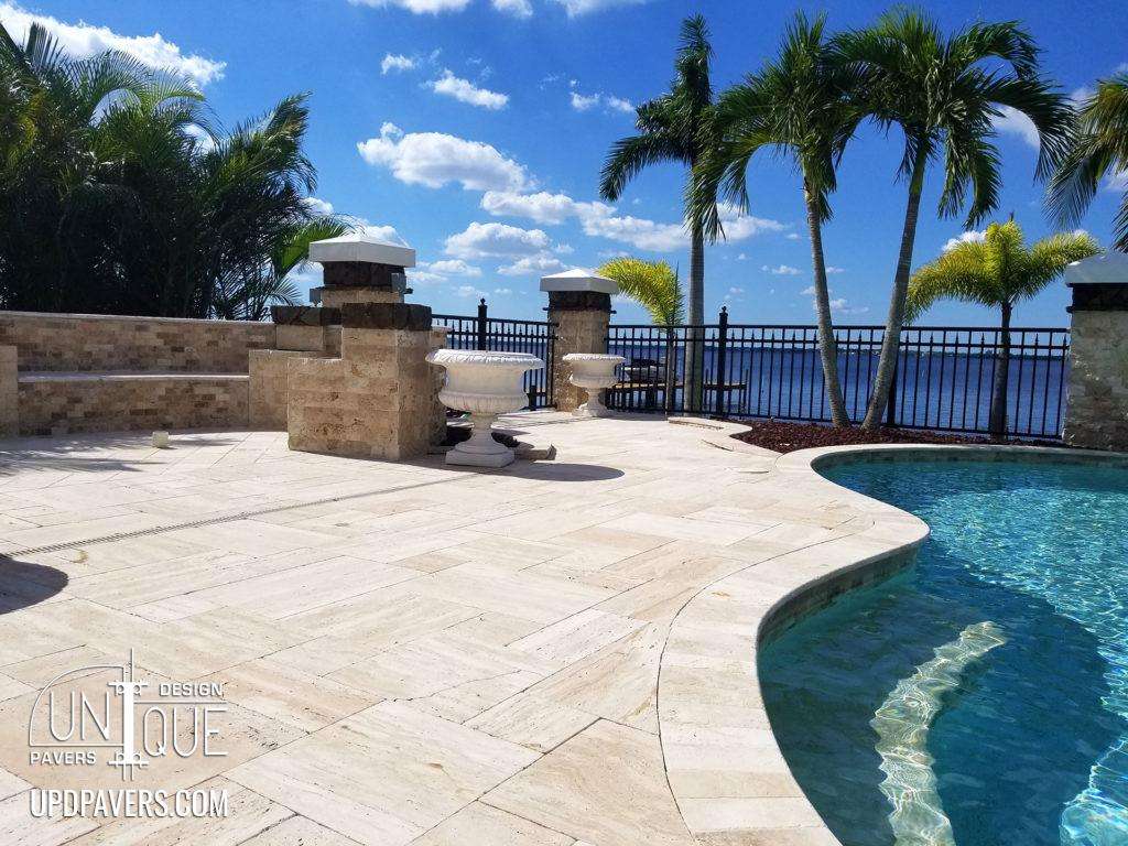 Luxurious poolside with pavers, palm trees, and waterfront view under a clear sky.
