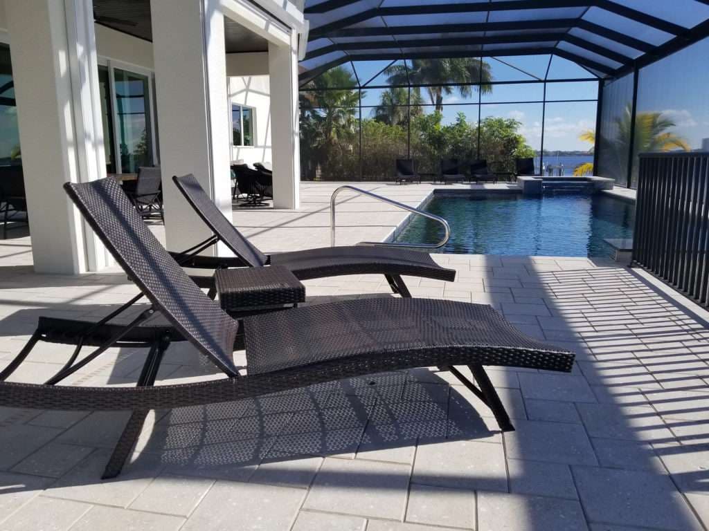 Lounge chairs by a pool in a screened patio with tropical scenery.