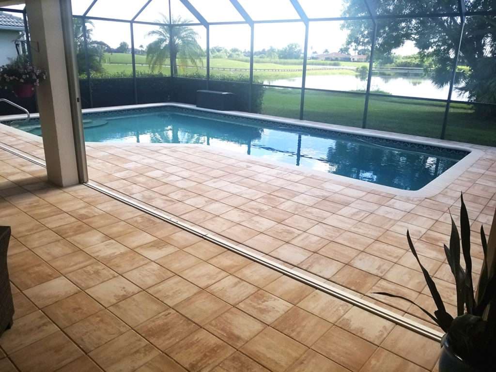 Modern backyard pool with sunlit tiled patio and scenic lake view through screened enclosure.