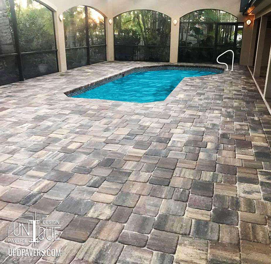 Stylish paver patio surrounding a blue pool with a modern design and lush greenery.