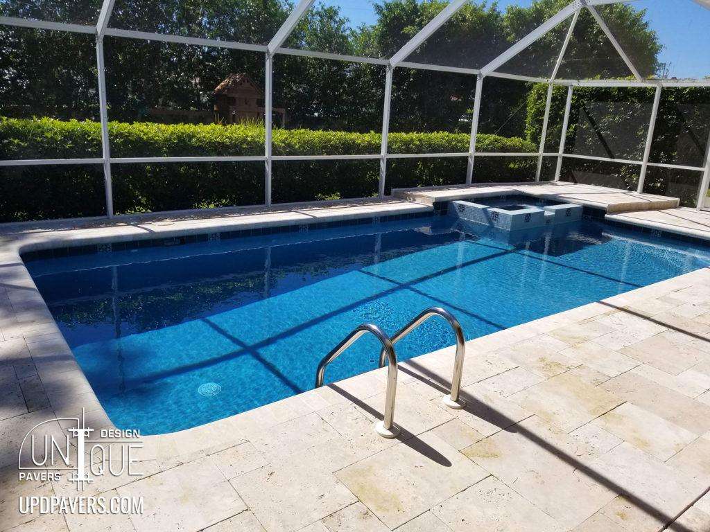 Modern backyard pool with stone patio and screened enclosure surrounded by greenery.