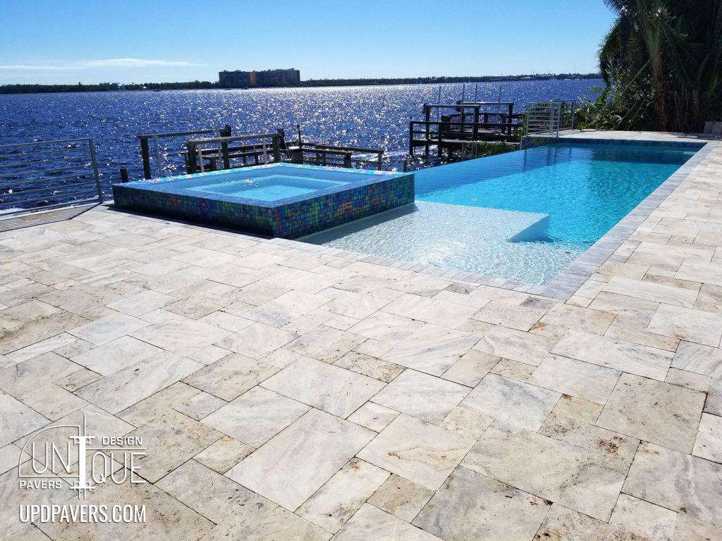 Luxury pool with spa overlooking waterfront, featuring modern stone pavers and scenic views.