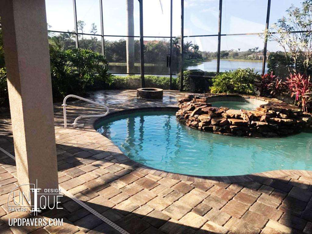 Luxury pool with stone spa and paver patio, surrounded by tropical landscaping and lake view.