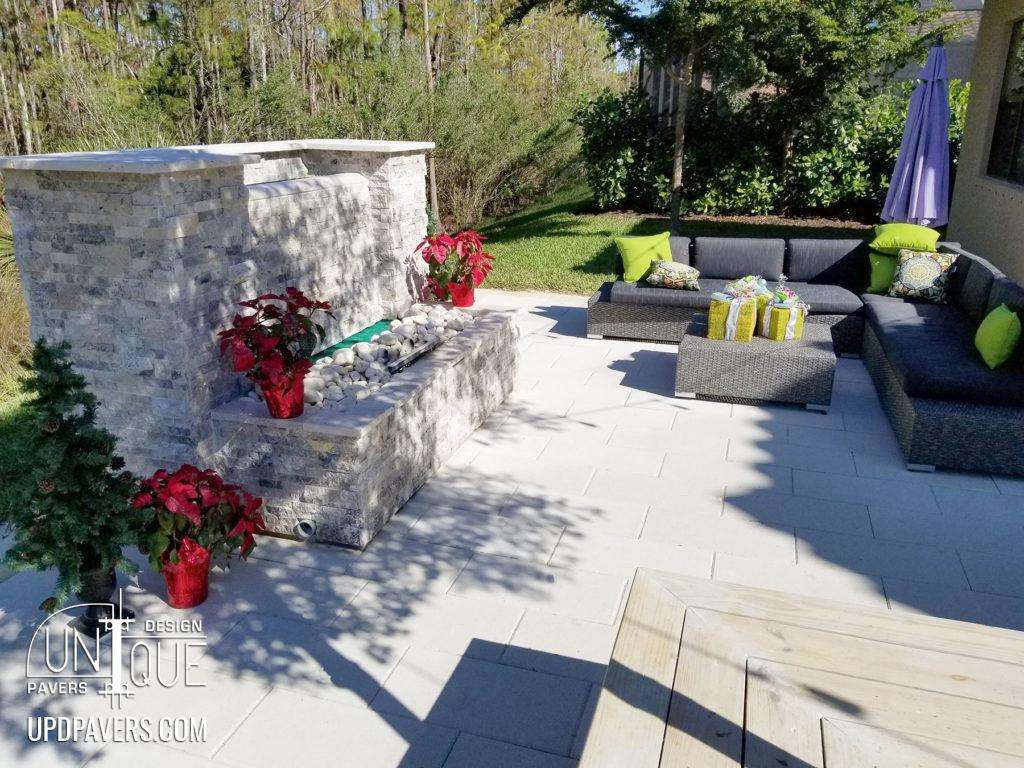 Modern outdoor lounge area with stone fireplace, comfortable seating, and vibrant plants.
