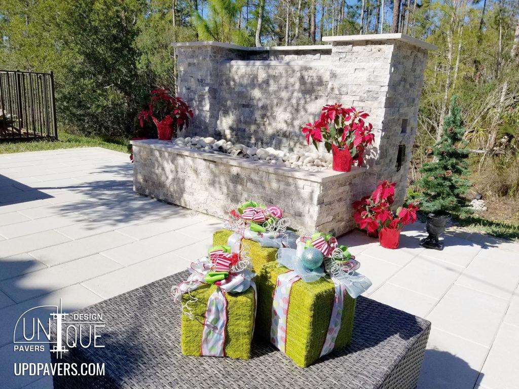 Outdoor holiday decor with wrapped gifts and a stone fireplace surrounded by greenery.