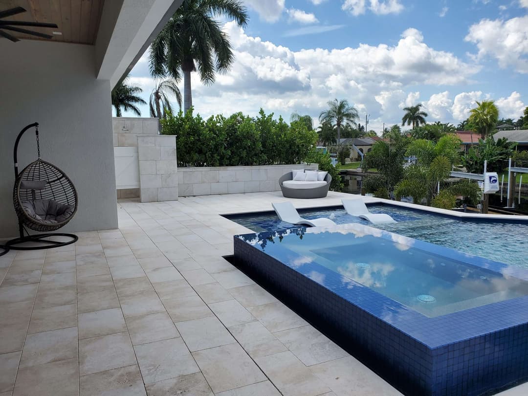 Luxurious patio with a pool, stylish lounge chairs, and tropical landscaping under a blue sky.