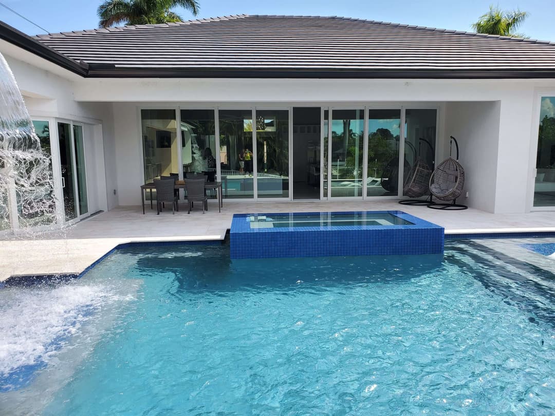 Luxurious poolside view featuring a spa, modern home, and spacious outdoor seating area.