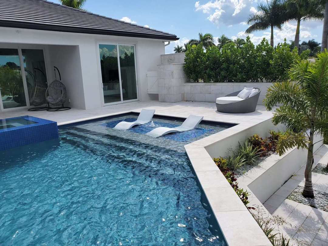 Modern backyard pool with lounge chairs, tropical landscaping, and sunny skies.