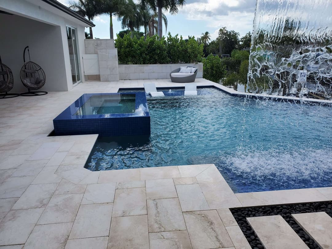 Luxury backyard pool with spa, water feature, and tropical landscaping in a sunny setting.