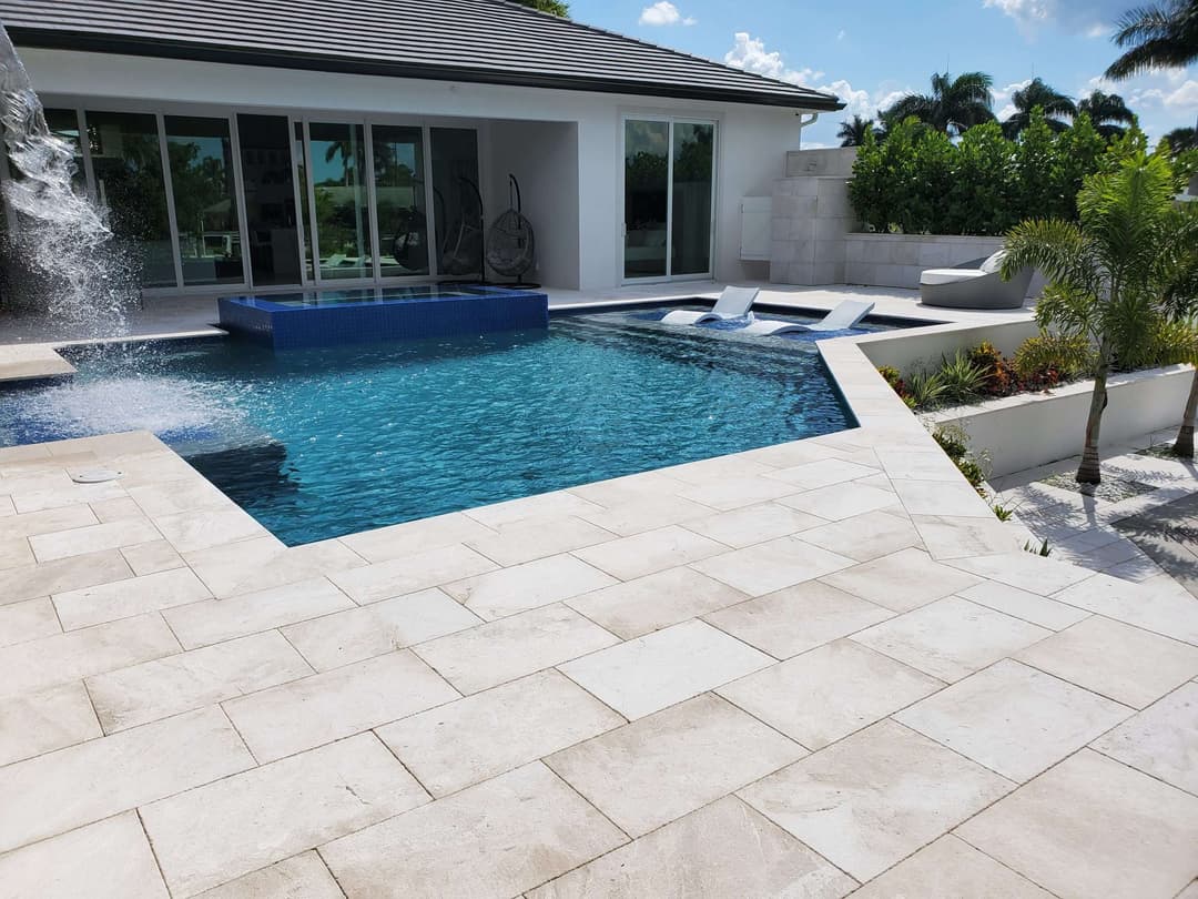 Luxury pool area with modern design, featuring blue water and lounge chairs in sunny setting.
