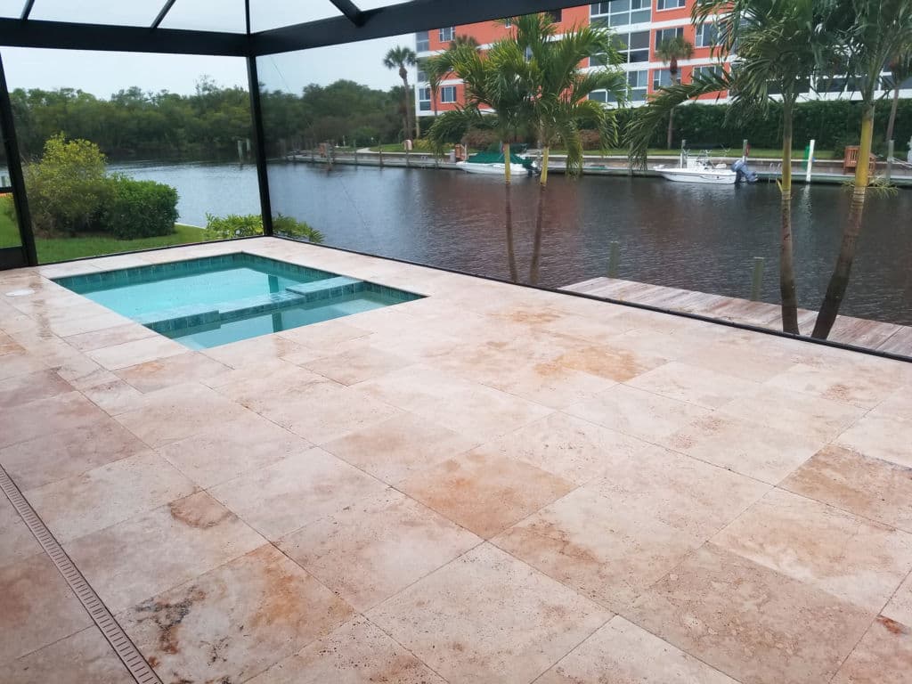 Luxurious pool area with travertine tiles, overlooking a serene canal and palm trees.