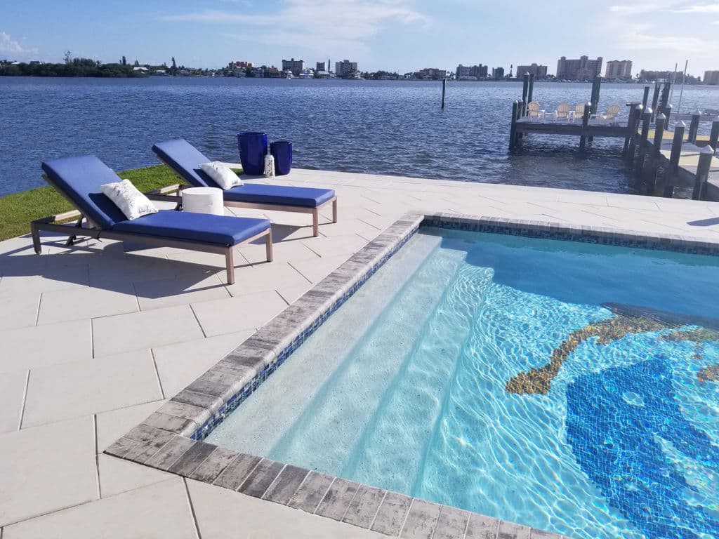 Luxury waterfront pool with loungers and scenic views of the water and skyline.