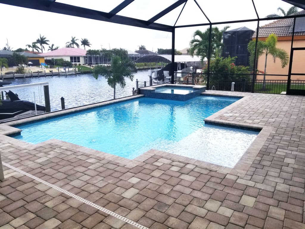 Luxury backyard pool with spa, screened enclosure, and water views in a tropical setting.