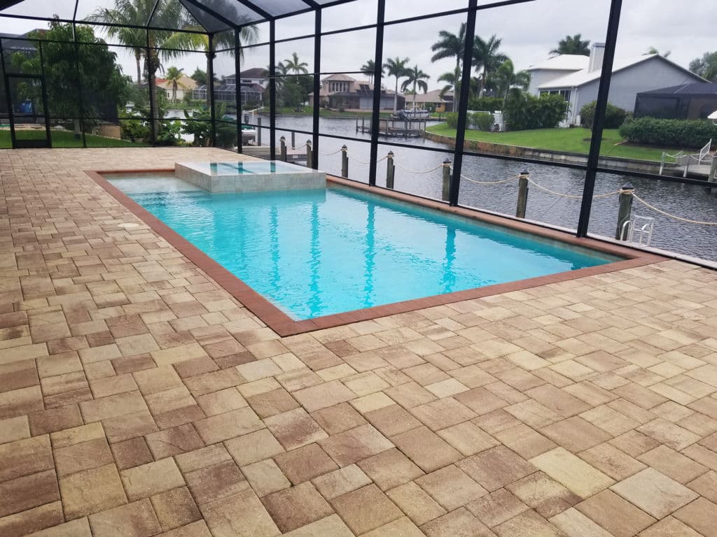 Stylish pool in a screened enclosure, surrounded by paver stones and water views.