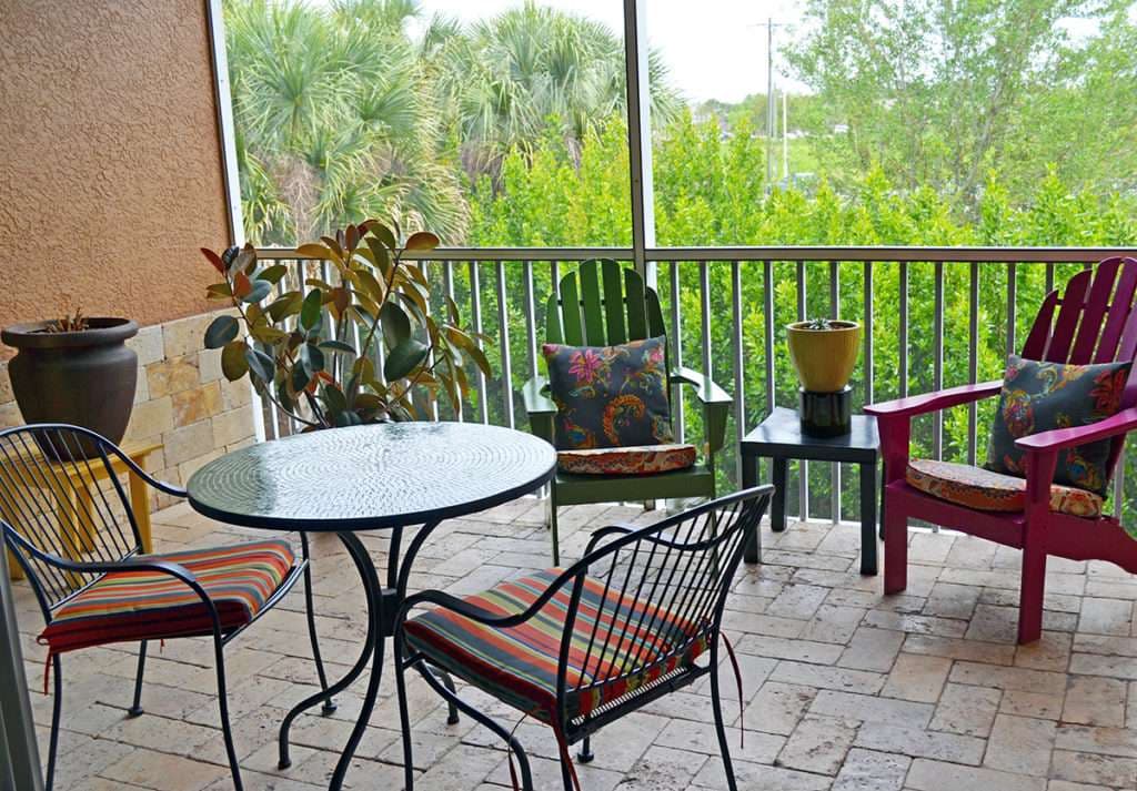 Cozy outdoor patio with colorful chairs, a table, and potted plants amidst lush greenery.