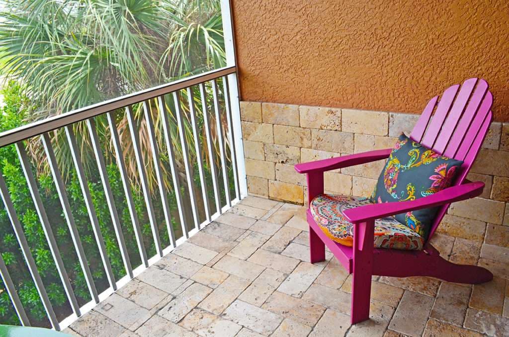 Colorful pink adirondack chair with patterned cushion on a balcony surrounded by greenery.