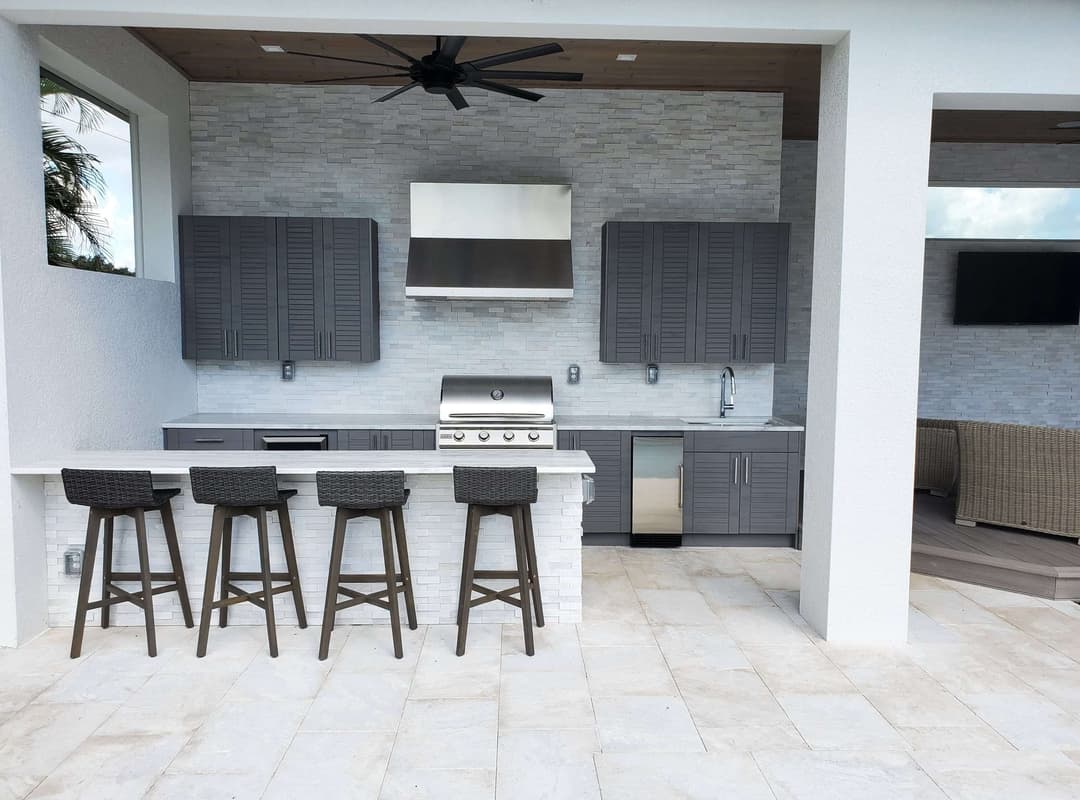 Modern outdoor kitchen with gray cabinetry, stainless steel appliances, and bar seating.