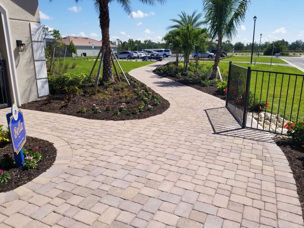 Paved walkway with decorative landscaping and a gated entrance to a home.