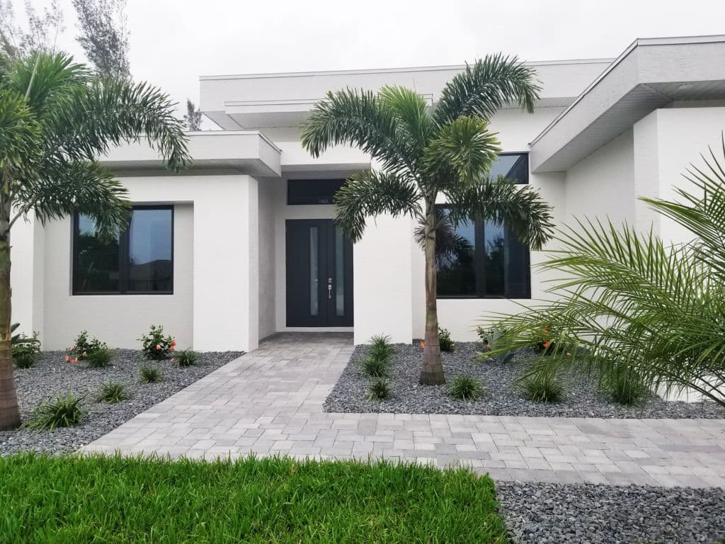 Modern white home entrance with palm trees, pavers, and landscaped gardens.