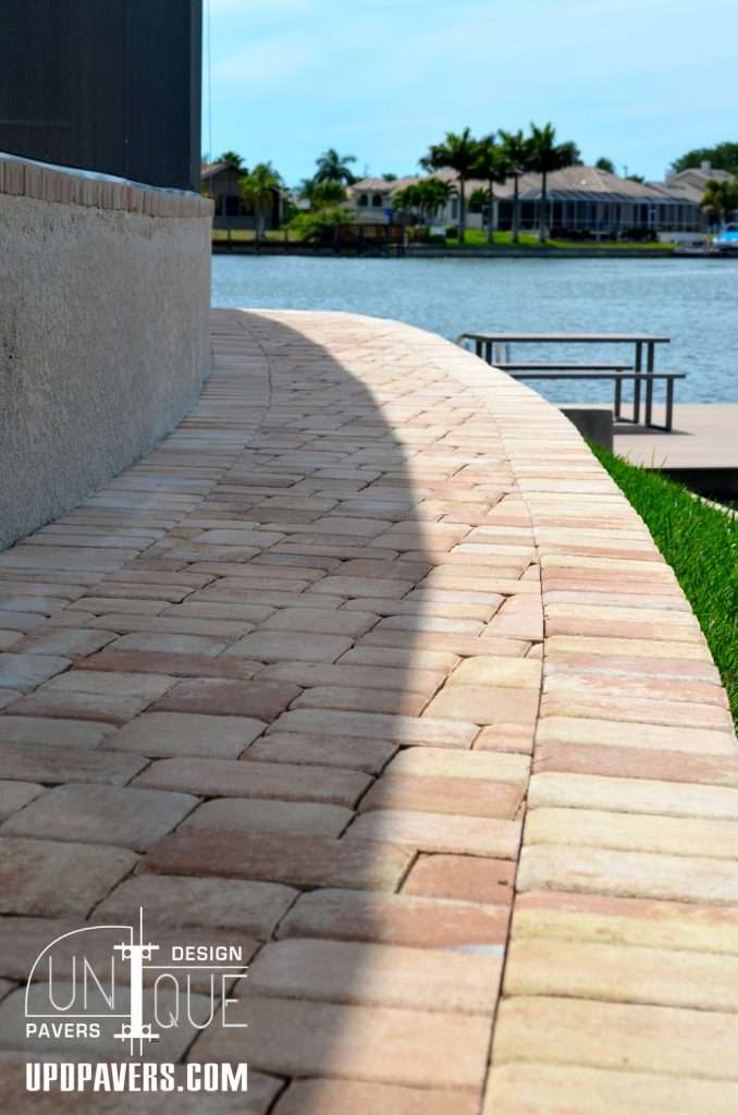 Curved brick pathway by a lake with palm trees, enhancing outdoor design aesthetics.