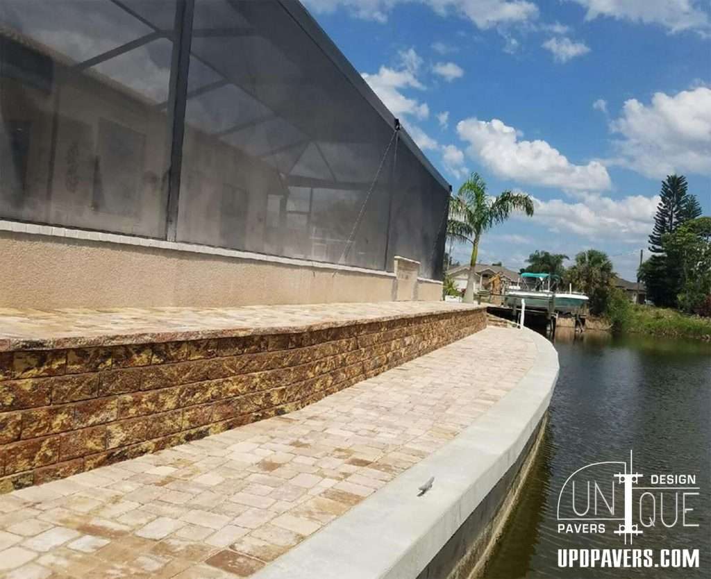 Paver patio by a serene waterfront with a screened enclosure and landscaping.