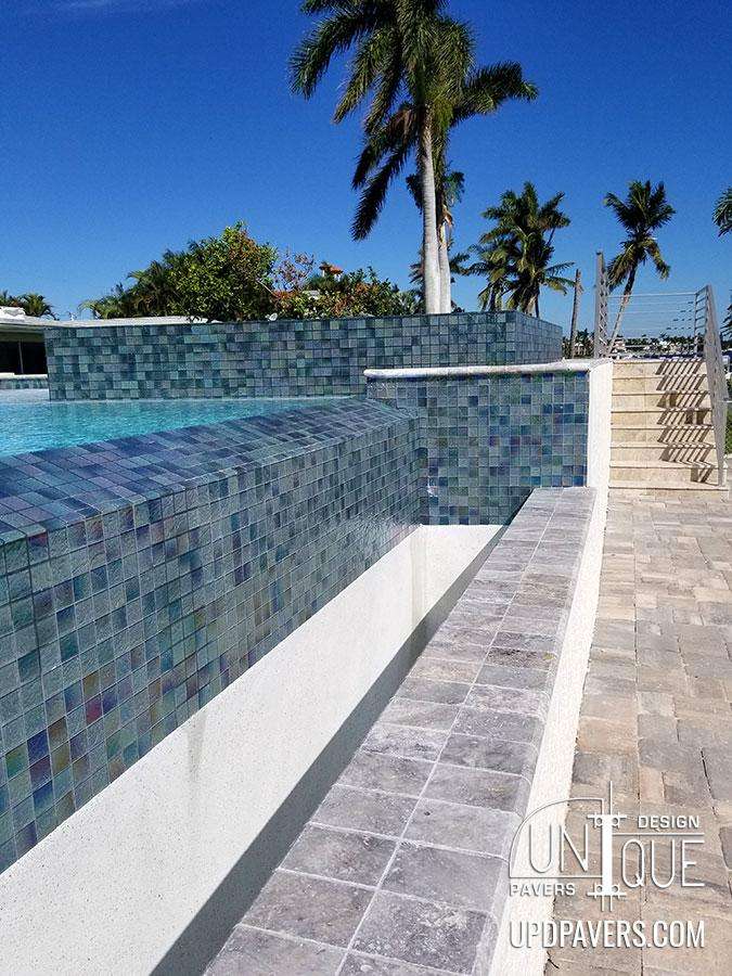 Modern pool design with mosaic tiles and a scenic palm-lined landscape.