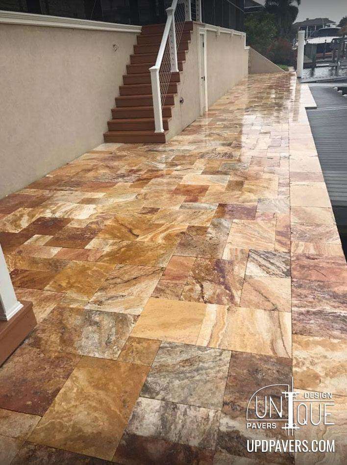 Stone patio with patterned pavers leading to a staircase by water, showcasing elegant design.
