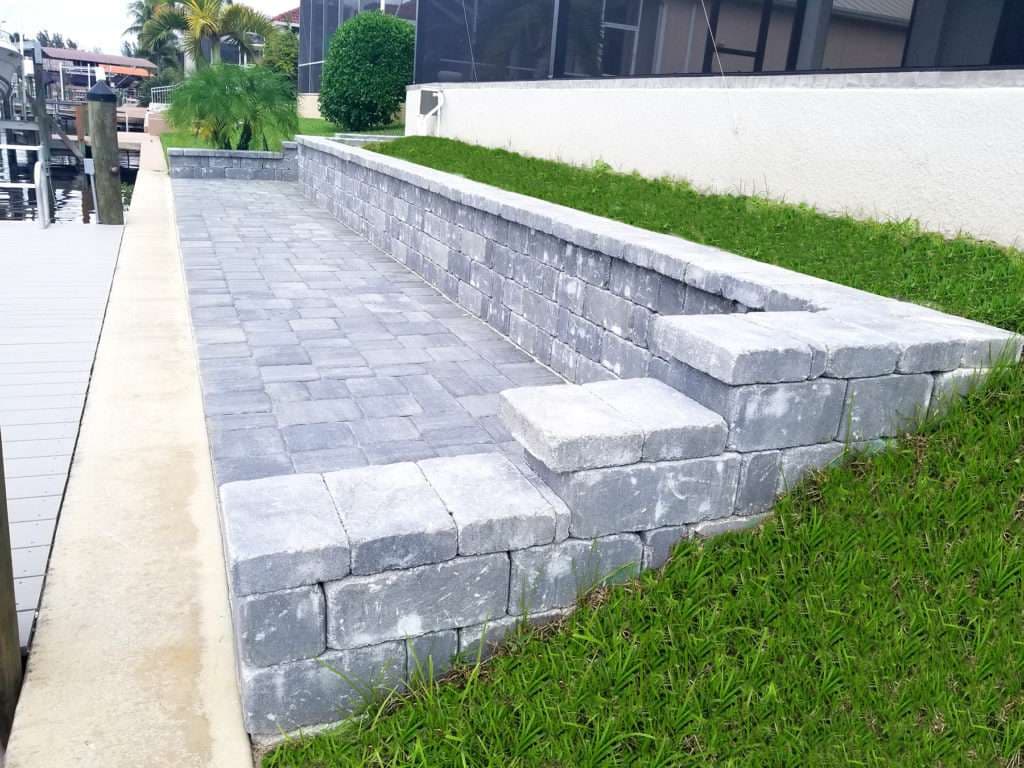 Outdoor stone patio with steps, grass, and waterfront in a landscaped area.