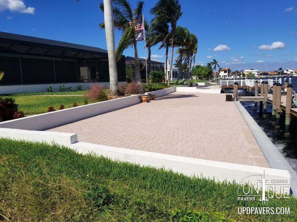 Modern paver patio by the water with palm trees and a clear blue sky. Ideal for outdoor gatherings.