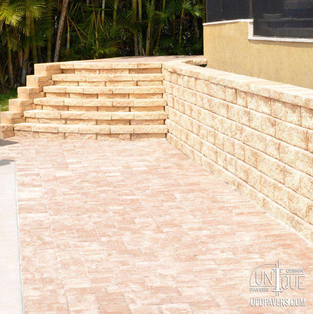 Paver stone patio with steps and retaining wall in a landscaped outdoor setting.