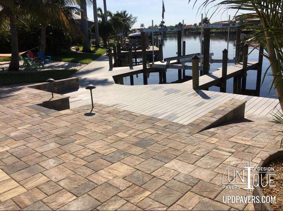 Paver patio by the water with dock, palm trees, and serene waterfront view.