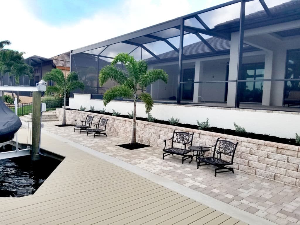 Modern outdoor seating area beside a waterway, featuring paver stones and green landscaping.