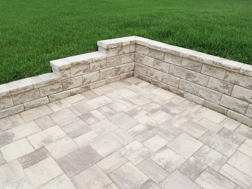 Paved patio area with stone wall and green grass background for outdoor landscaping.