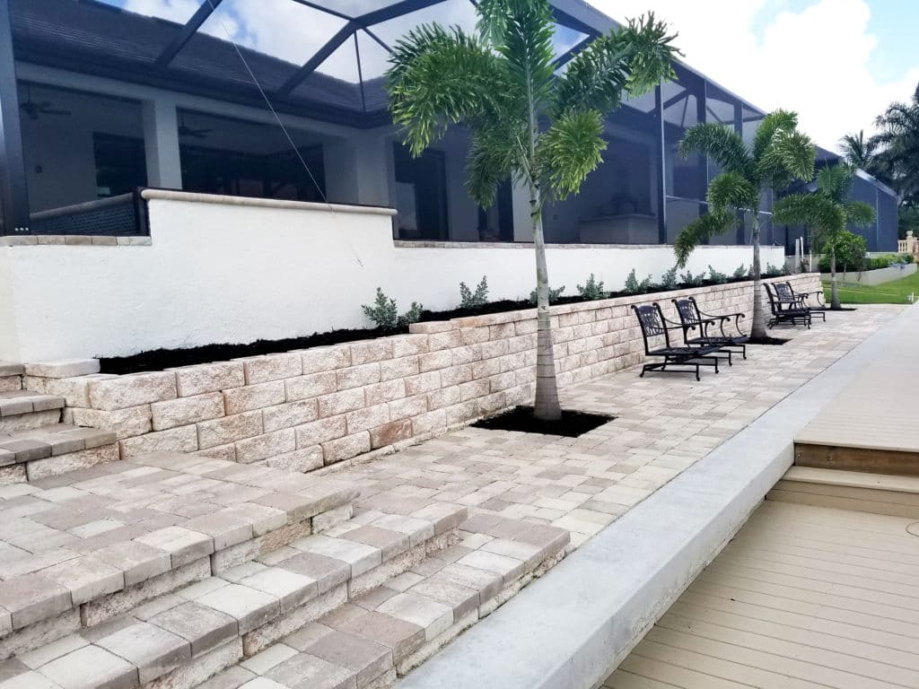 Patio area featuring stone steps, palm trees, and seating along a landscaped wall.