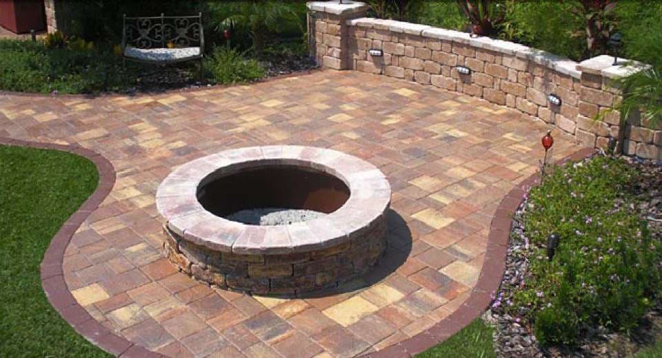 Outdoor patio with stone fire pit surrounded by pavers and lush landscaping.