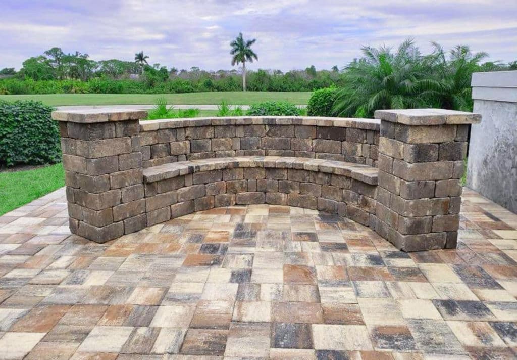 Curved stone seating area on a patio with patterned paver flooring and green landscaping.