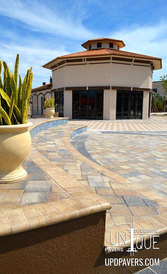 Modern paved outdoor area featuring a round building and decorative plants under a blue sky.