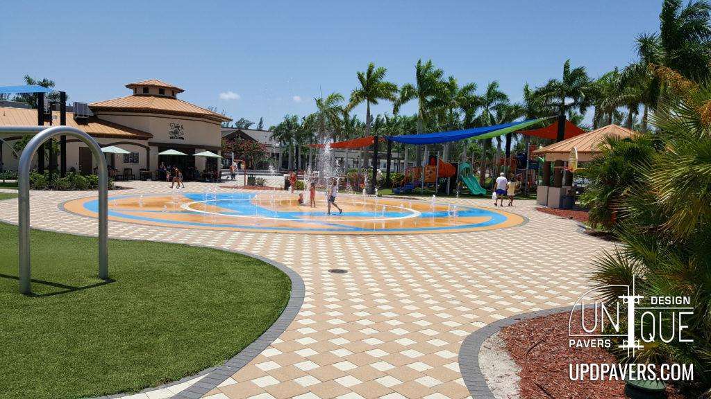 Children playing in a colorful splash pad at a family-friendly park with palm trees.