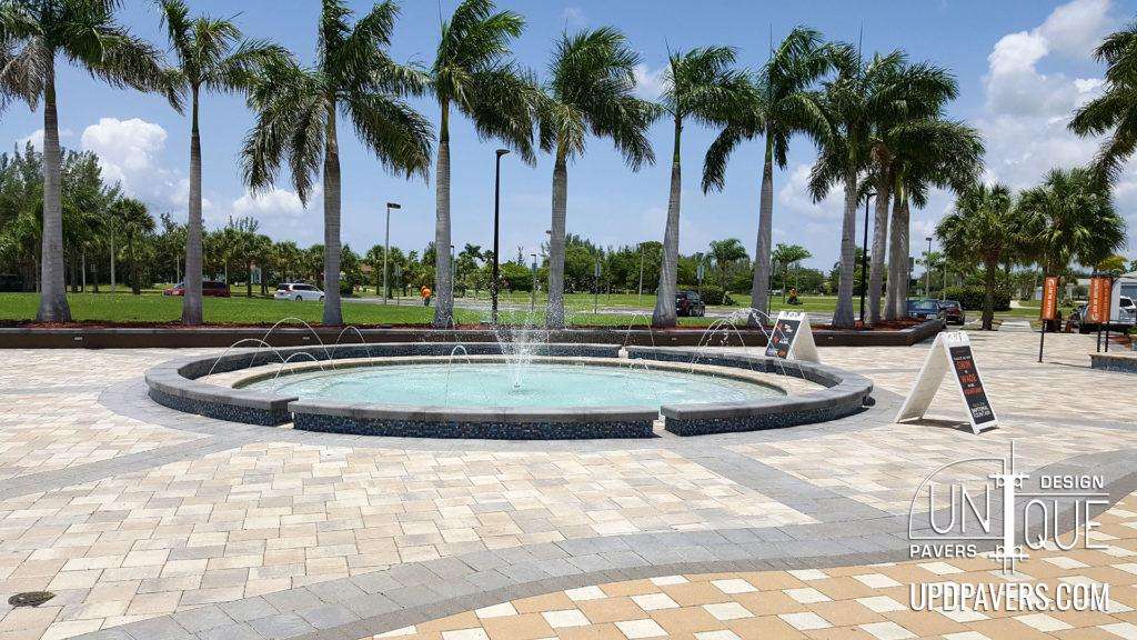 Fountain surrounded by palm trees in a landscaped outdoor plaza. Unique Pavers design.