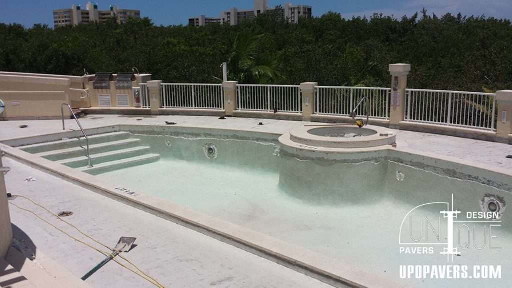 Renovated swimming pool with hot tub, surrounded by a modern fence and lush greenery.