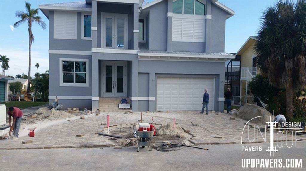 Newly paved driveway installation outside a modern grey house with palm trees.
