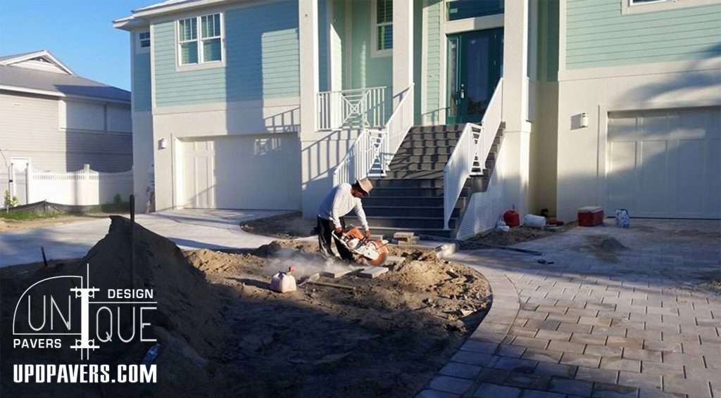 Worker using a concrete saw to install pavers outside a residential home.