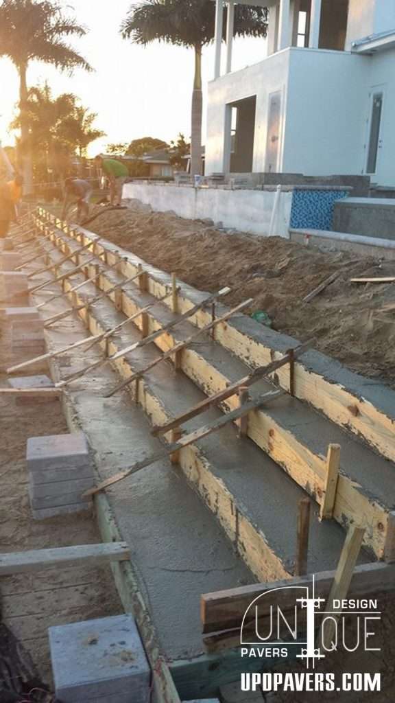Concrete paver installation process with wooden forms and construction site at sunset.