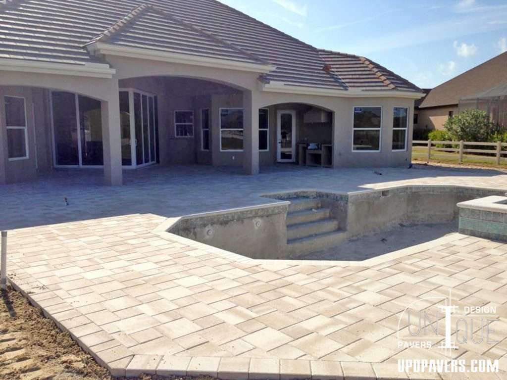 Paved patio and pool area with modern home exterior and sunny sky backdrop.