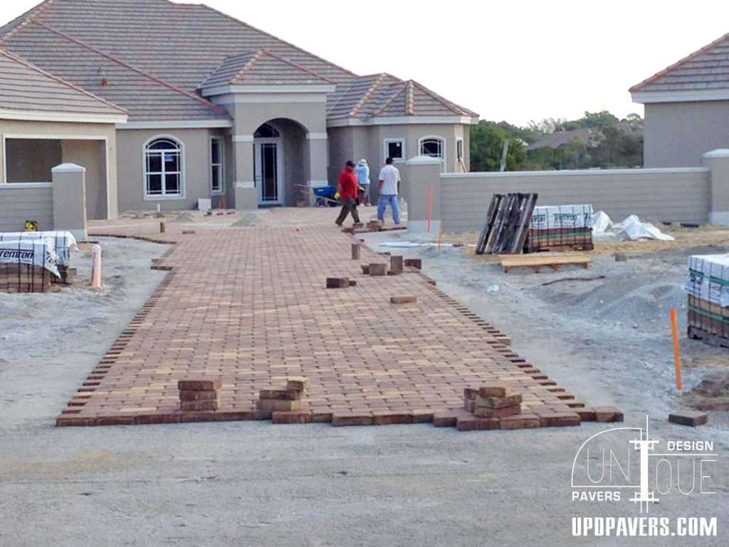 Brick paver installation in front of a home, with workers and construction materials visible.