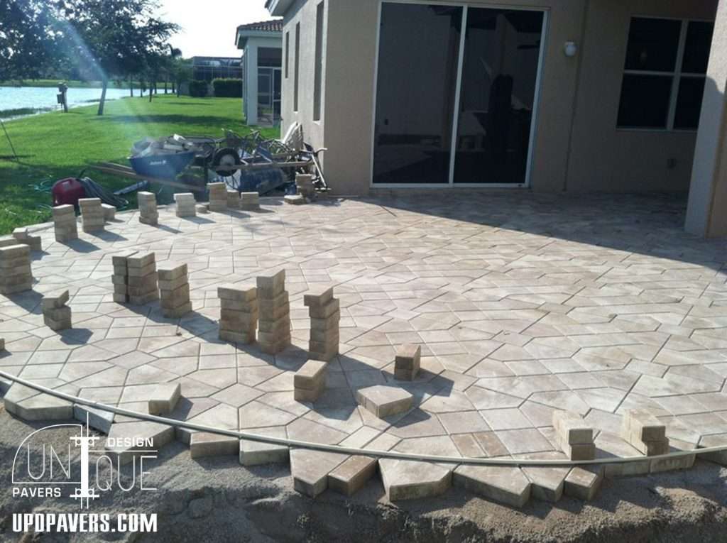 Paver patio installation in progress with stacked bricks and a scenic lake view.
